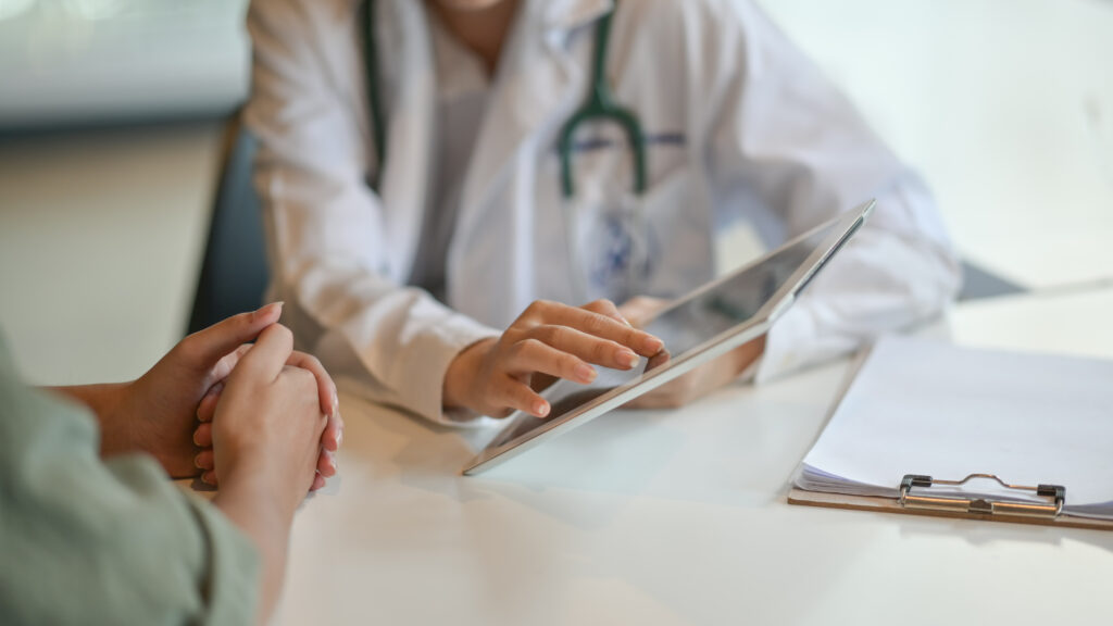 Arzt spricht mit einer Patientin und zeigt Daten auf einem Tablet.